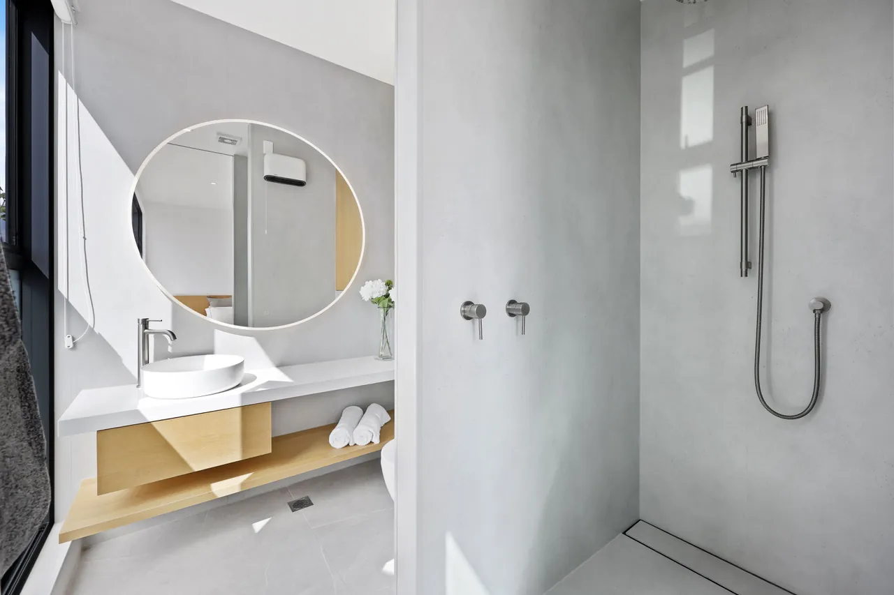 A bathroom at Penthouse 505 with a walk-in shower, stone vanity and round mirror