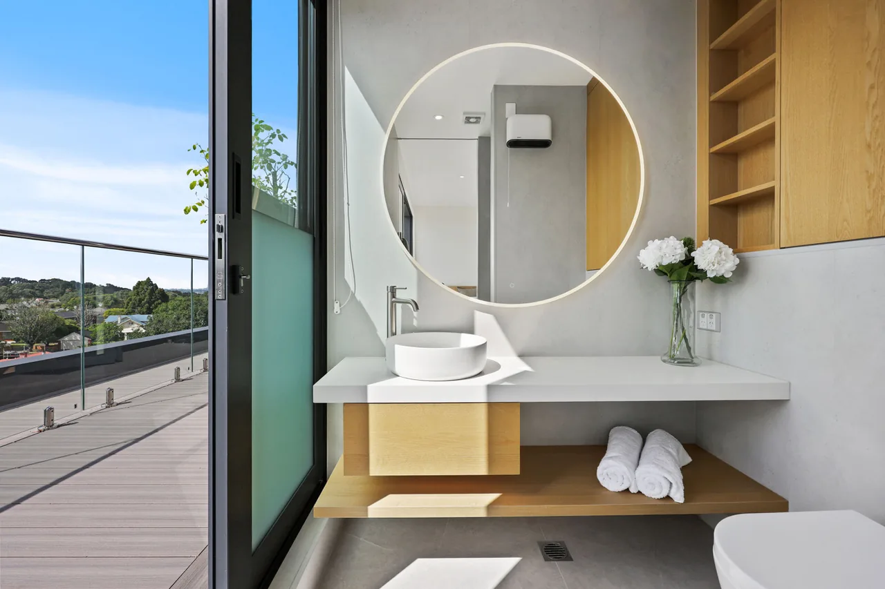 The ensuite at Penthouse 505, oak vanity beneath a round backlit mirror, with the terrace beyond