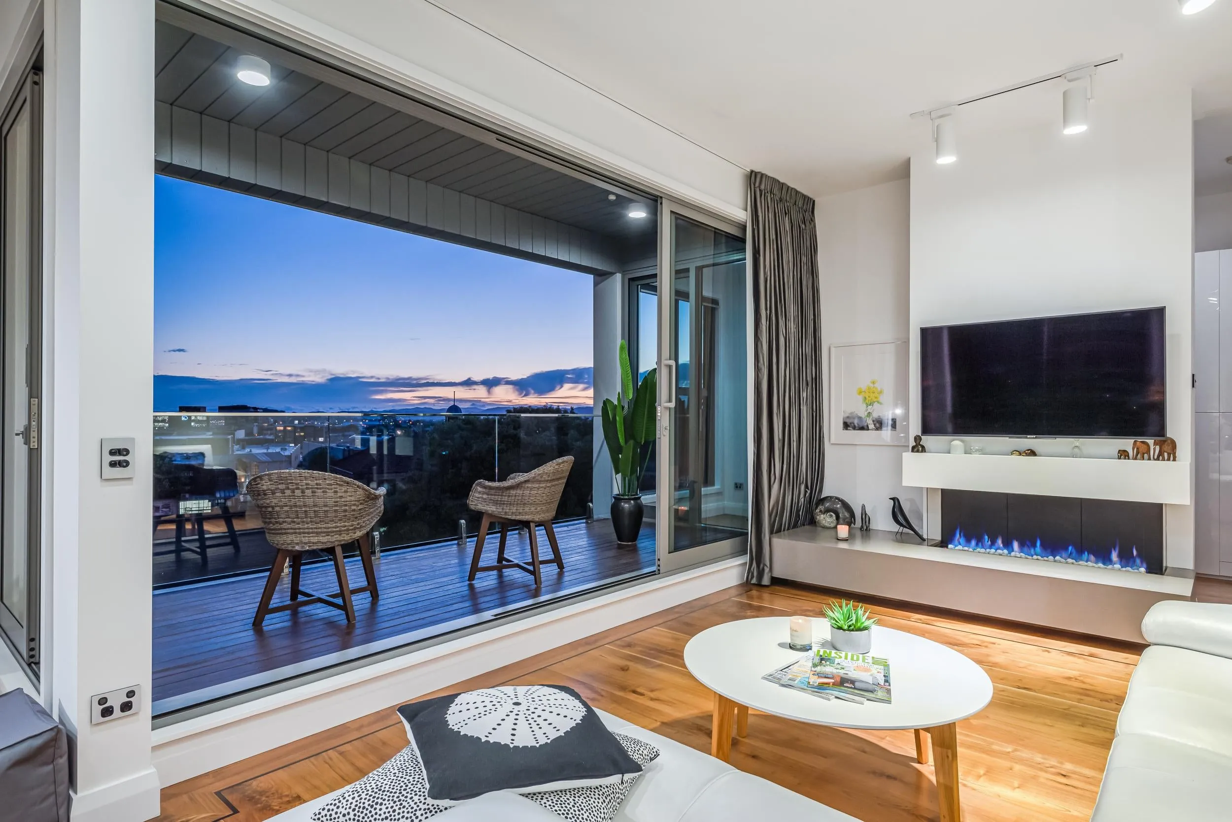 The upstairs lounge of Penthouse 504 at dusk, sliders open to the deck and the gas fire lit